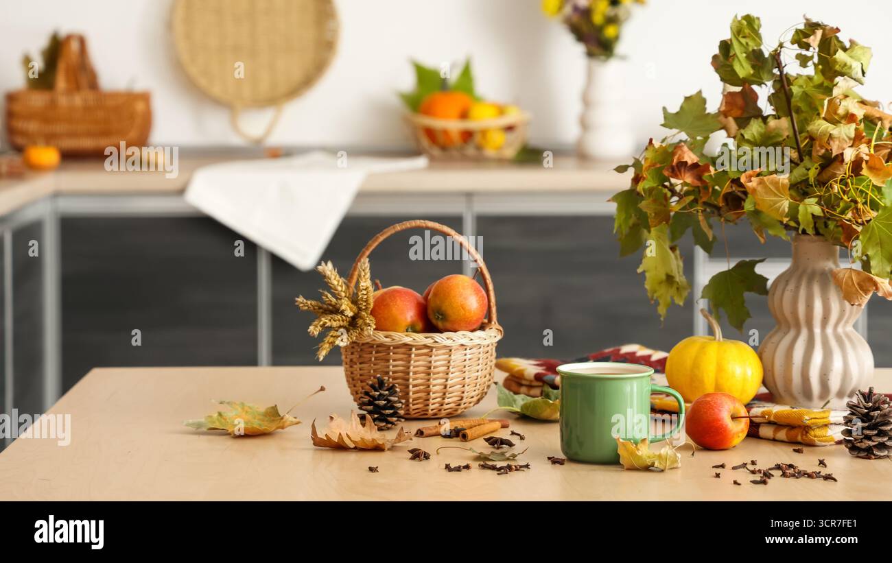 Vase avec des feuilles d'automne, tasse de thé chaud, panier avec des pommes et des épices sur la table dans la cuisine Banque D'Images