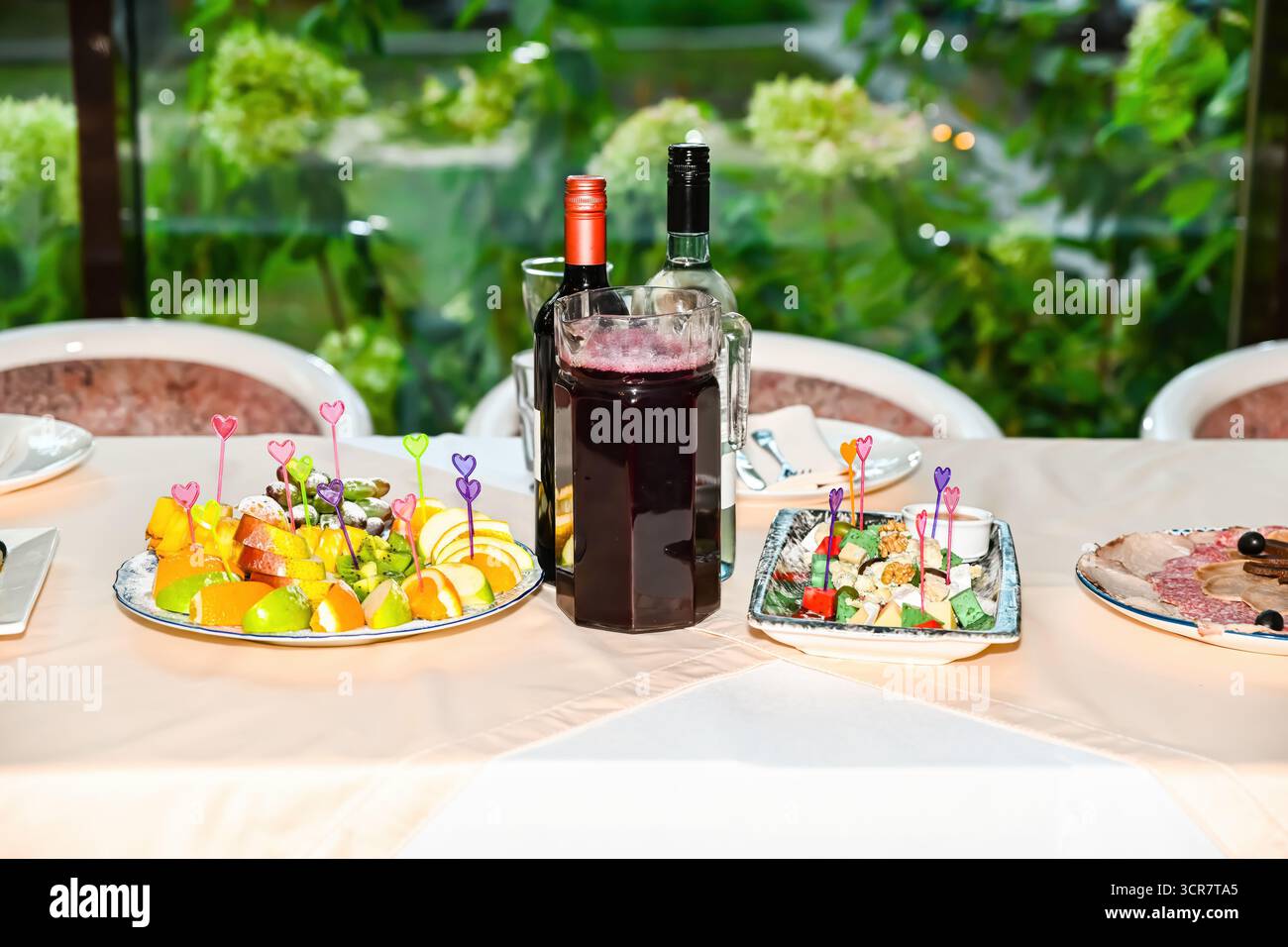 Table de fête avec plateau de fruits, collations variées, vin rouge et boisson aux baies dans un pichet en verre, prêt pour la célébration ou la fête avec espace de copie Banque D'Images