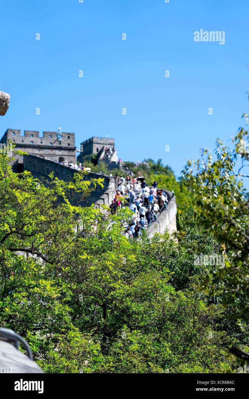 Pékin, Chine - 18 septembre 2025 : des foules de visiteurs explorent une ancienne fortification en pierre, serpentant à travers des montagnes luxuriantes sous un ciel bleu clair Banque D'Images