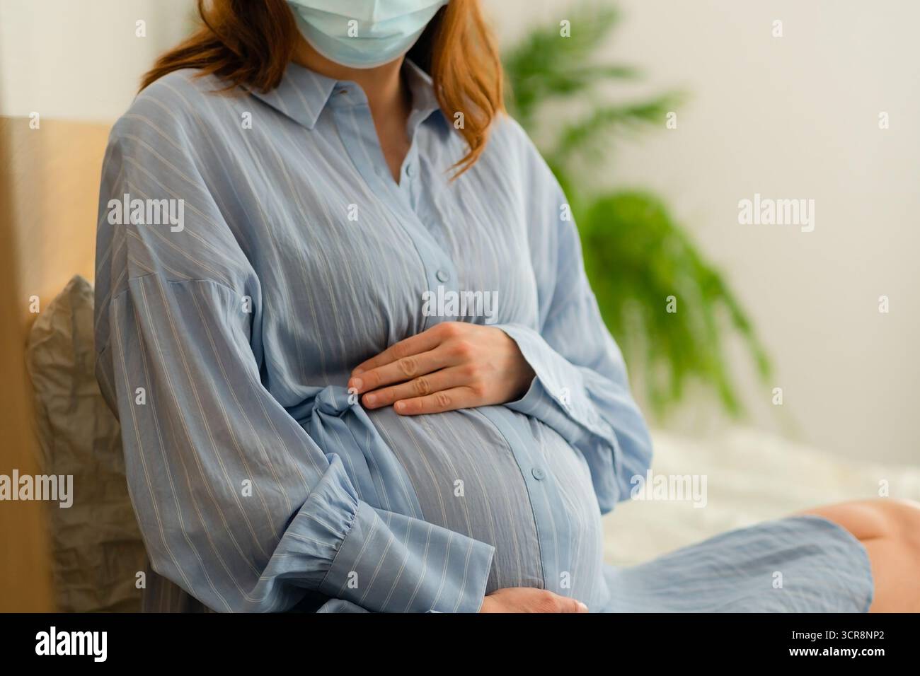 Future mère portant un masque de protection au repos au lit. Gérer les symptômes de la maladie de manière responsable pendant la grossesse. Banque D'Images