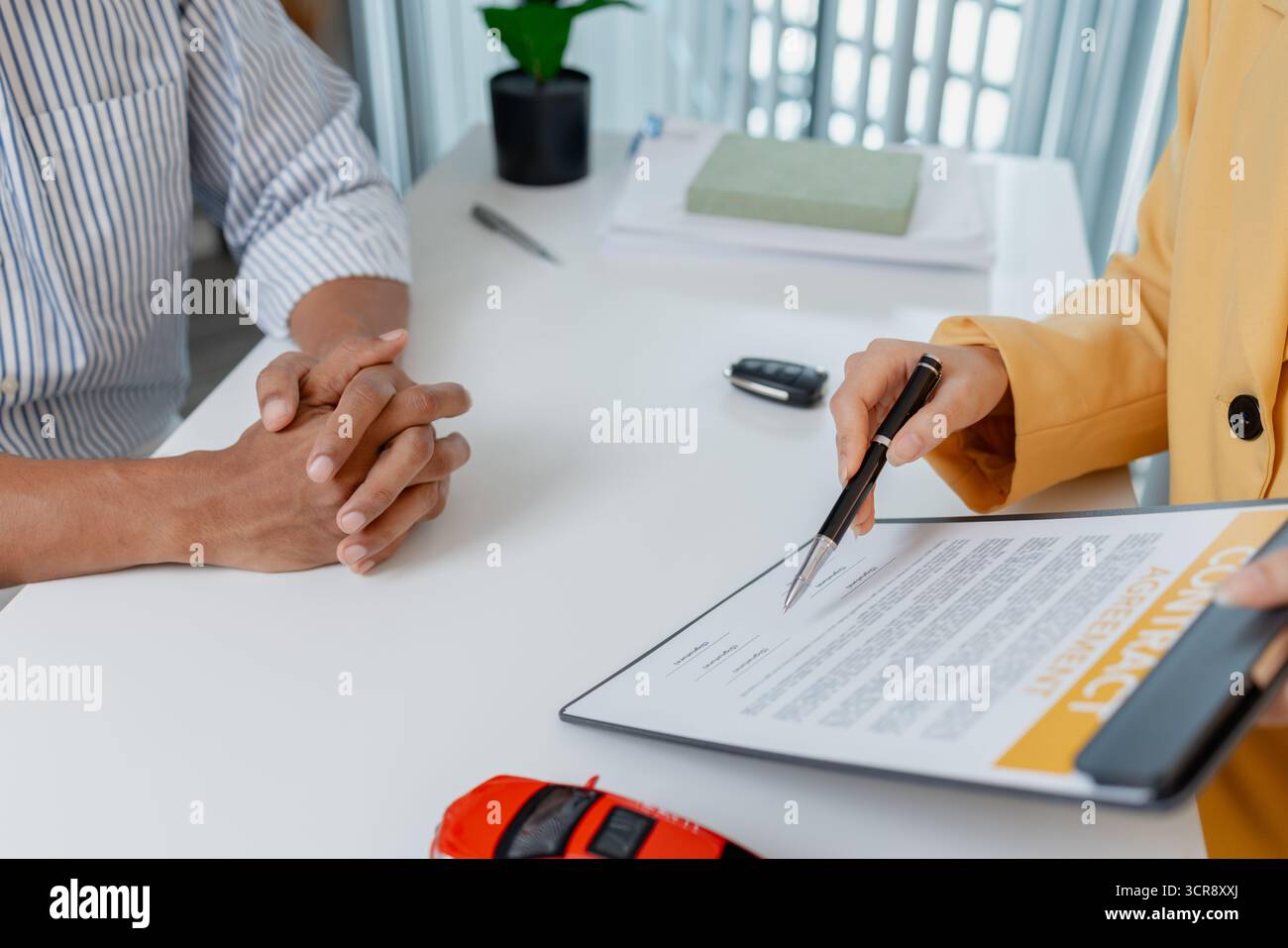 Une négociation de vente de voitures a lieu dans un bureau où une vendeuse dans un blazer jaune explique les détails d'un contrat à un client masculin, Showin Banque D'Images