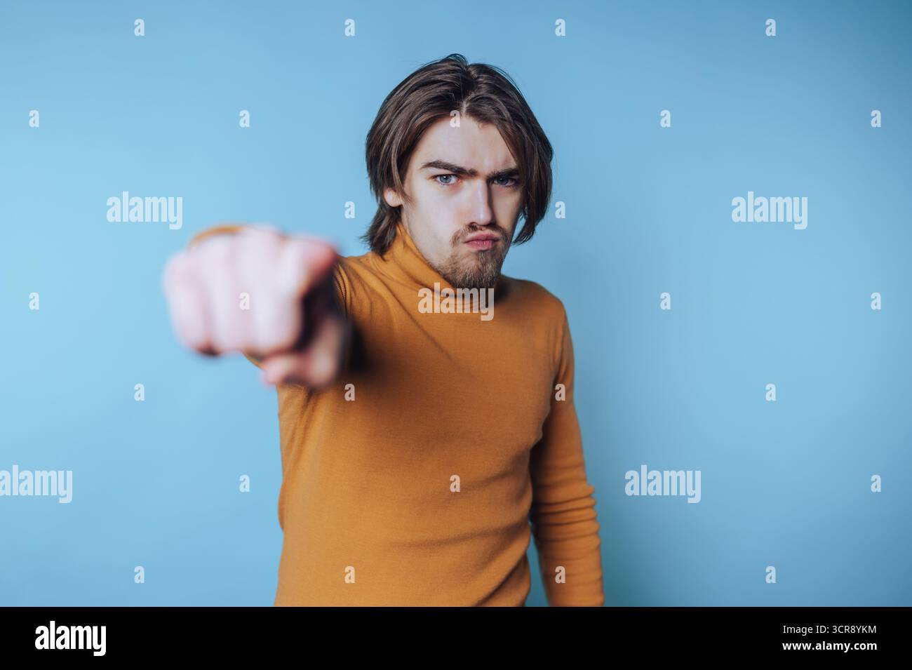Jeune homme avec de longs gestes de cheveux avec confiance sur un fond bleu dans une pose expressive représentant l'affirmation de soi Banque D'Images