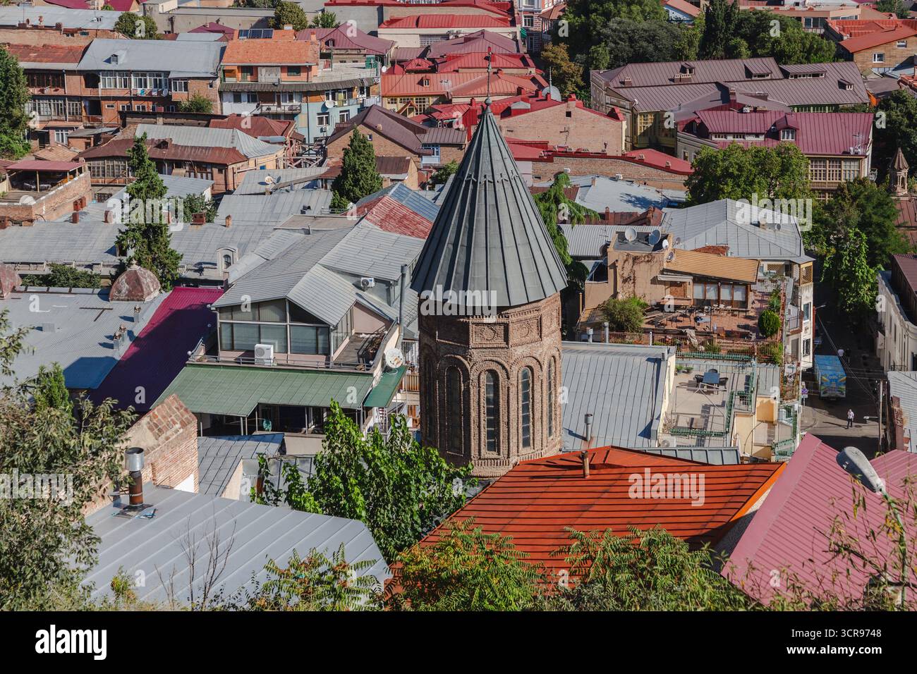 Vue sur la flèche conique de l'église Metekhi s'élève grandiose, un phare parmi les toits en terre cuite et la végétation luxuriante, se prélasser dans la lumière du jour sereine, Tbilissi, Tbilissi, Géorgie. Banque D'Images