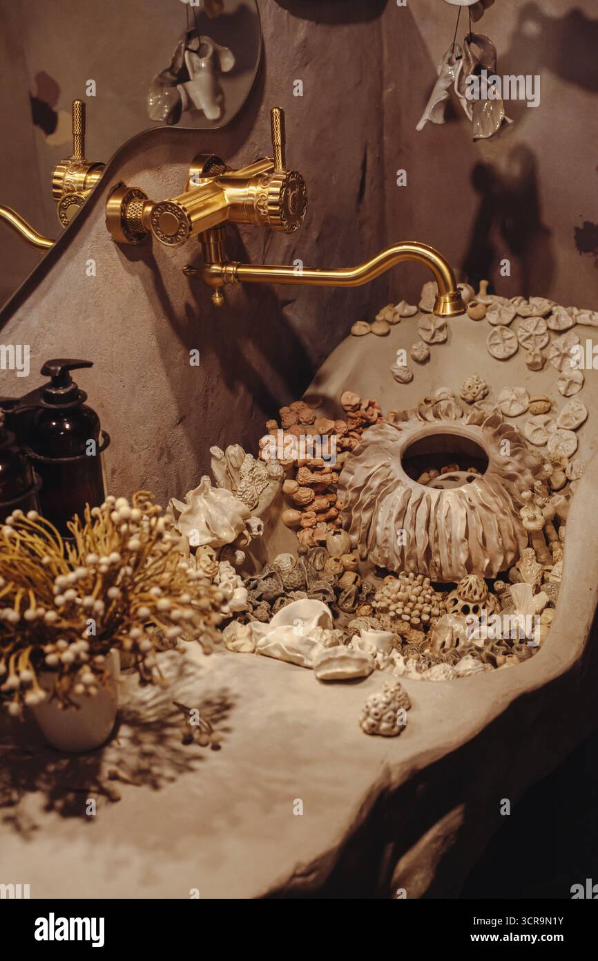 Un évier unique est rempli de divers coquillages, pierres et décor naturel, créant une atmosphère tranquille. Les robinets en or ajoutent une touche d'élégance à th Banque D'Images
