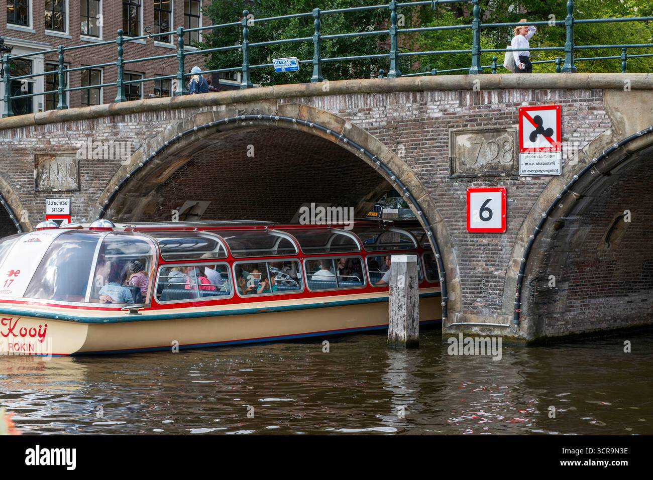 Amsterdam, pays-Bas - 5 août 2025 : un bateau panoramique glisse sur les canaux historiques d'Amsterdam sous un pont de pierre. Banque D'Images