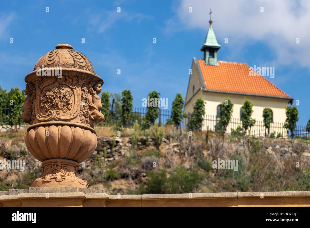 Vase ornemental en pierre et pittoresque petite église sur la colline contre le ciel bleu d'été, Prague, Tchéquie Banque D'Images