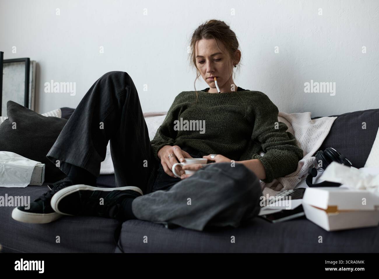 Dans un salon sombre, une jeune femme est assise sur un canapé, perdue dans ses tristes pensées. Banque D'Images