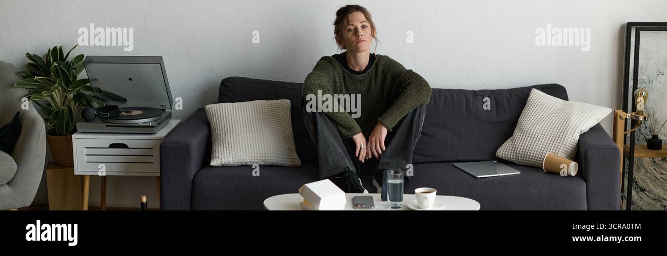 Une jeune femme est assise tranquillement sur un canapé dans son salon, réfléchissant à ses sentiments de solitude. Banque D'Images