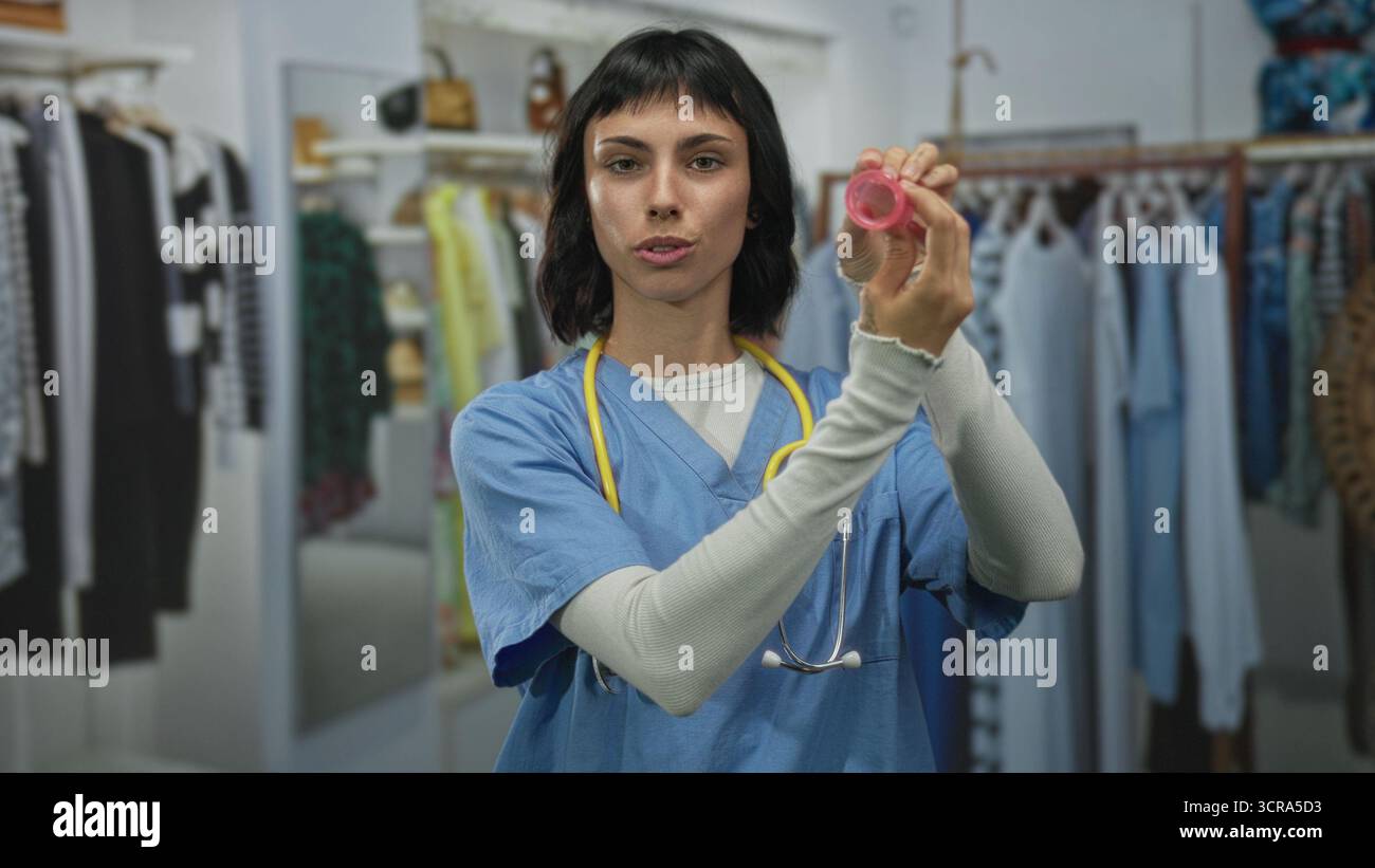 Femme infirmière tient une coupe menstruelle rose dans un bâtiment de magasin de détail démontrant son utilisation et souriant ; sensibilisation à l'autonomisation. Banque D'Images