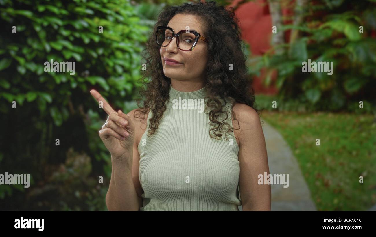 Femme hispanique portant des lunettes pointe doigt dans le parc vert urbain ; avertissement conseils d'instruction d'orientation. Banque D'Images