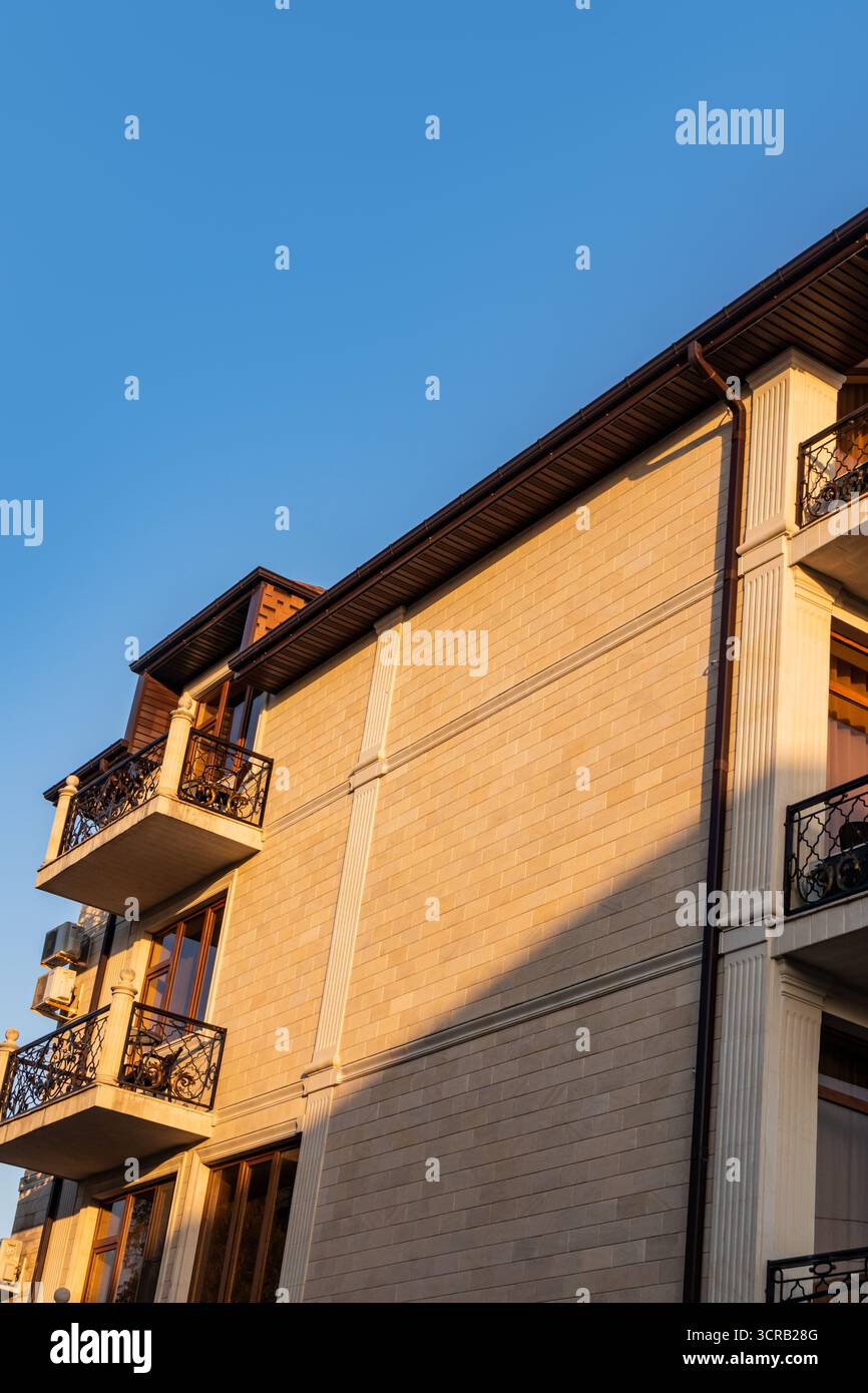 Un fragment d'une partie du beau mur latéral d'un immeuble résidentiel avec des balcons en verre élégants enveloppés dans les rayons du soleil Banque D'Images