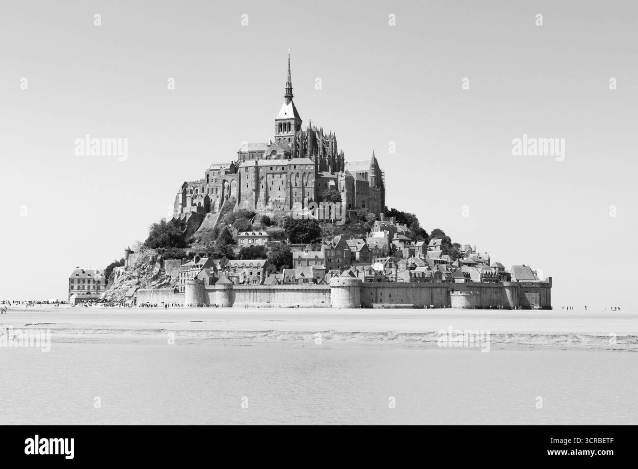 Image en échelle de gris d'une vue dégagée sur le Mont-Saint-Michel, toute l'île autoportée sur le sable environnant contre un ciel dégagé. Angle bas. Banque D'Images