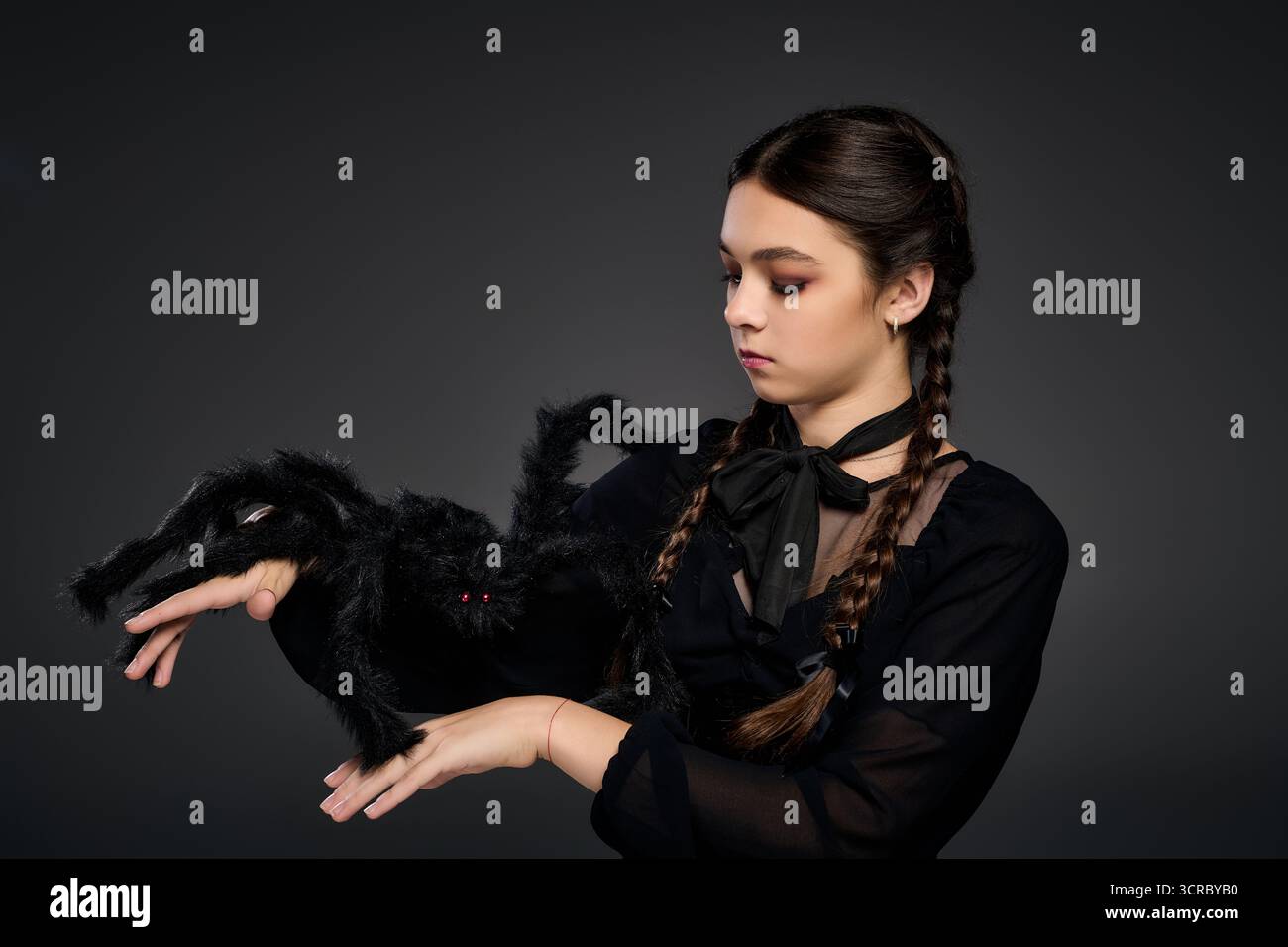 Une fille habillée comme un personnage gothique pose avec un accessoire d'araignée effrayant pendant Halloween. Banque D'Images