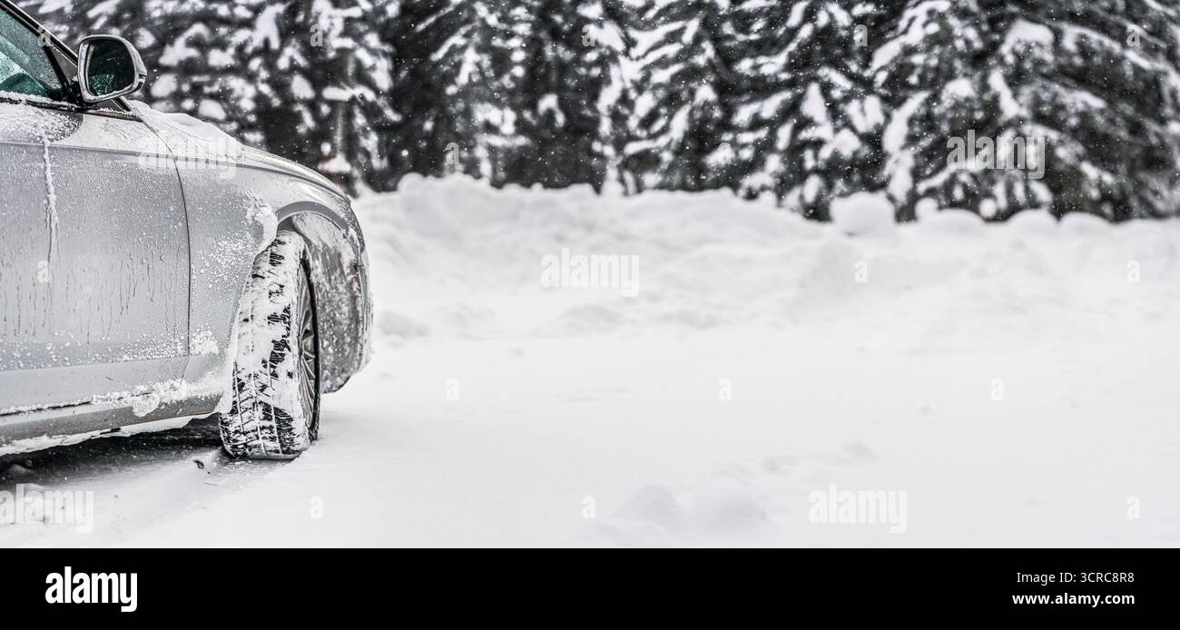 Voiture argentée couverte de glace garée sur la route de neige, vue de détail sur le côté et la roue avant de derrière, arbres flous arrière-plan espace vide pour le texte à droite Banque D'Images