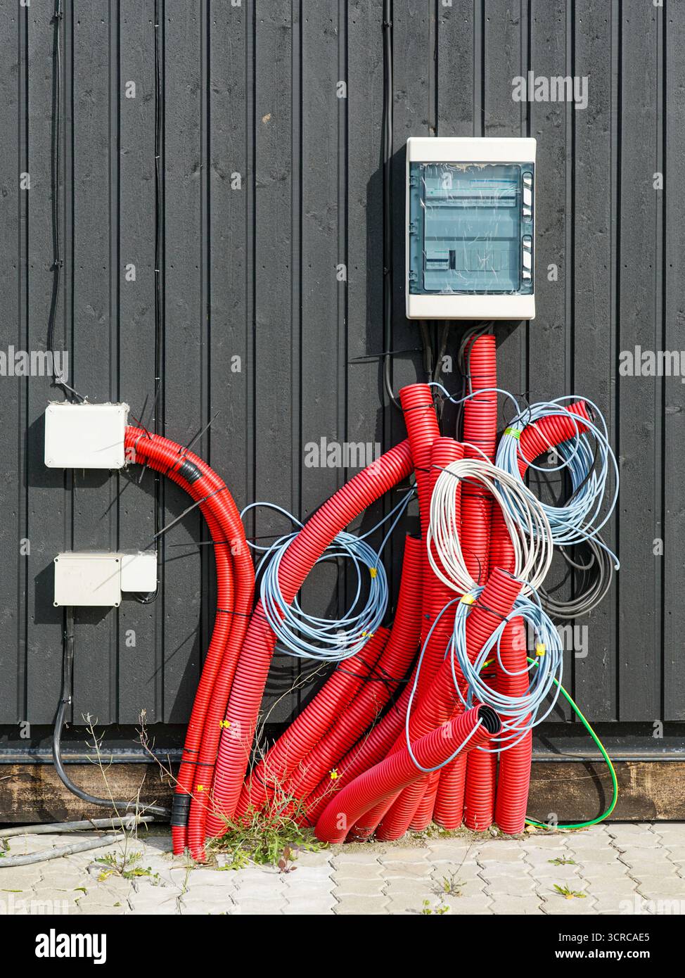 Installation électrique extérieure avec conduits rouges, câbles enroulés et boîte à fusibles montés sur un mur en bois noir Banque D'Images