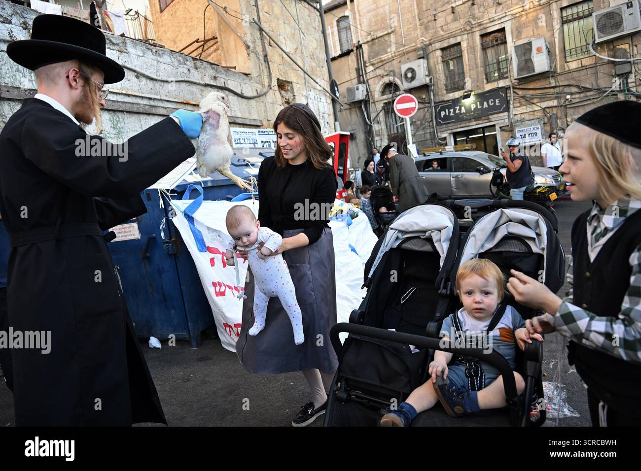 Jérusalem, Israël. 30 septembre 2025. Un homme juif ultra-orthodoxe balançant un poulet sur la tête d'un bébé tout en exécutant l'ancien rituel juif de Kapparot à Mea Shearim à Jérusalem, le mardi 30 septembre 2025. Le rituel Kapparot est exécuté avant Yom Kippour, le jour des Expiations, tandis que la personne prie en balançant un poulet sur sa tête, ce qui transfère symboliquement les péchés de l'année passée au poulet. Yom Kippour est le jour le plus Saint de l'année juive et commence au coucher du soleil le 1er octobre. Photo de Debbie Hill/ crédit : UPI/Alamy Live News Banque D'Images