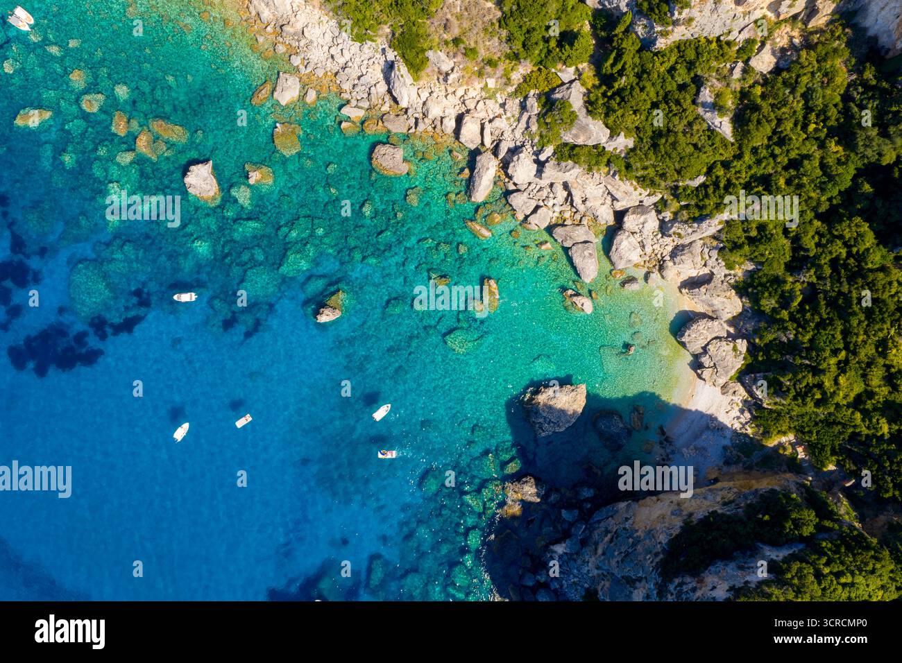 Paradise Found : une perspective aérienne de drone descendant d'une plage rocheuse secrète et d'une mer turquoise immaculée à Corfou, en Grèce. De petits bateaux flottent sur le cri Banque D'Images
