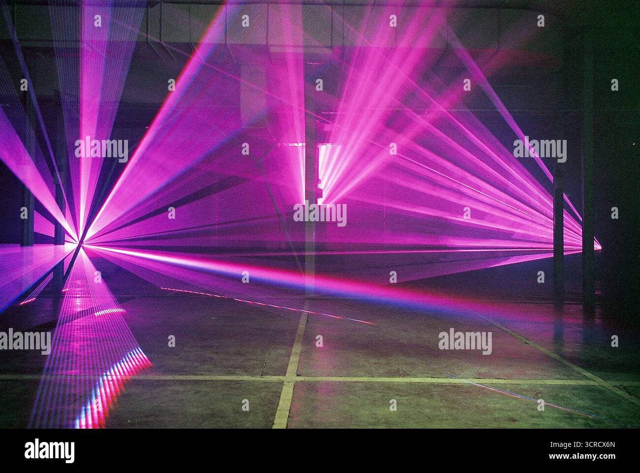 Photo de film analogique de faisceaux lumineux rouges et violets coupant à travers la brume dans un ensemble de garage. Les lasers s'étendent vers la caméra - surréaliste, graveleux, atmosphérique. Banque D'Images