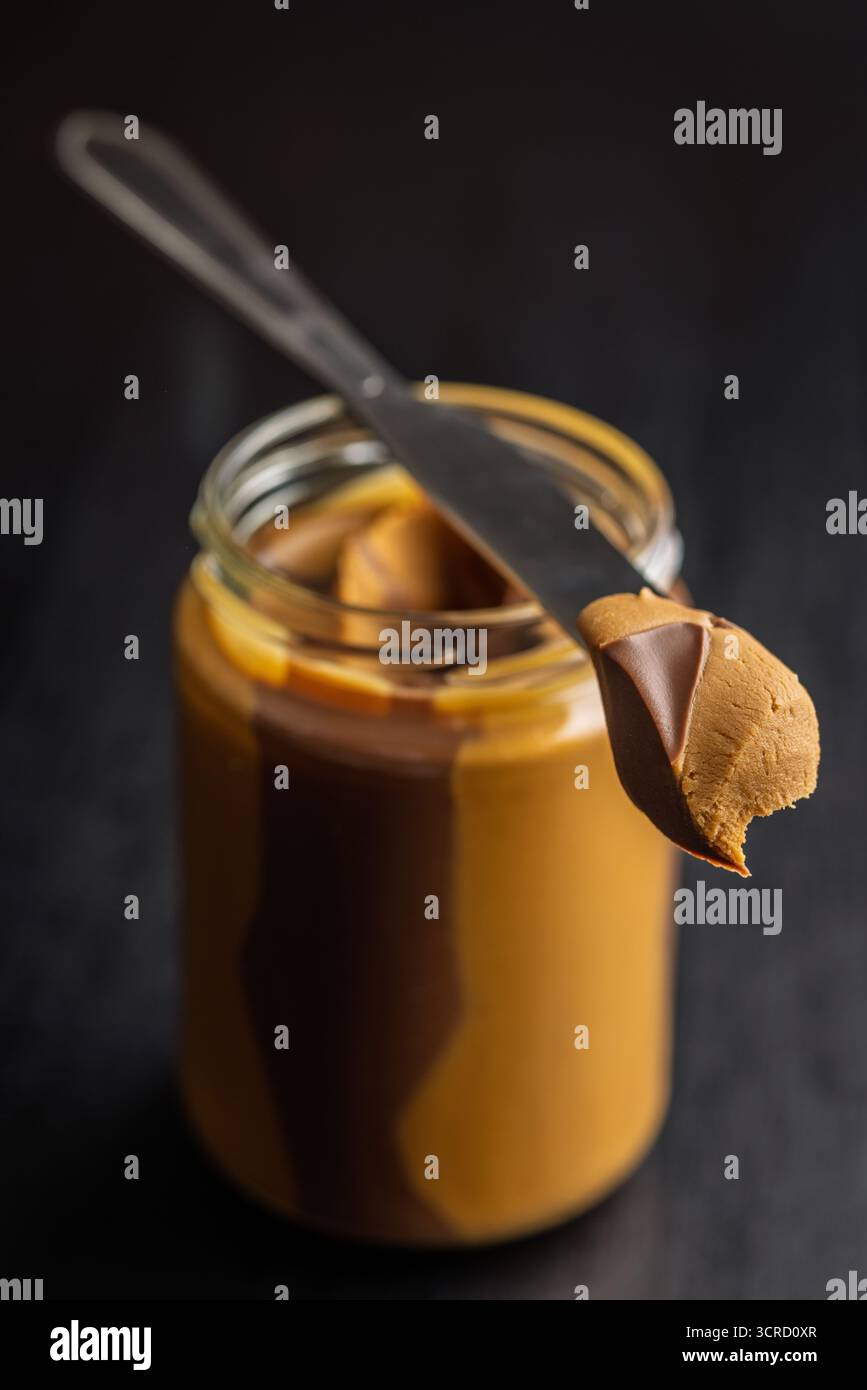 Tartiner au chocolat aux noix bicolore en pot sur une table noire. Banque D'Images