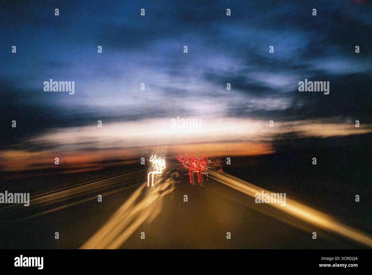 Exposition analogique longue depuis le siège du conducteur — autoroute floue au coucher du soleil, déformée et brumeuse, comme à travers les yeux d’un conducteur ivre ou haut. Banque D'Images