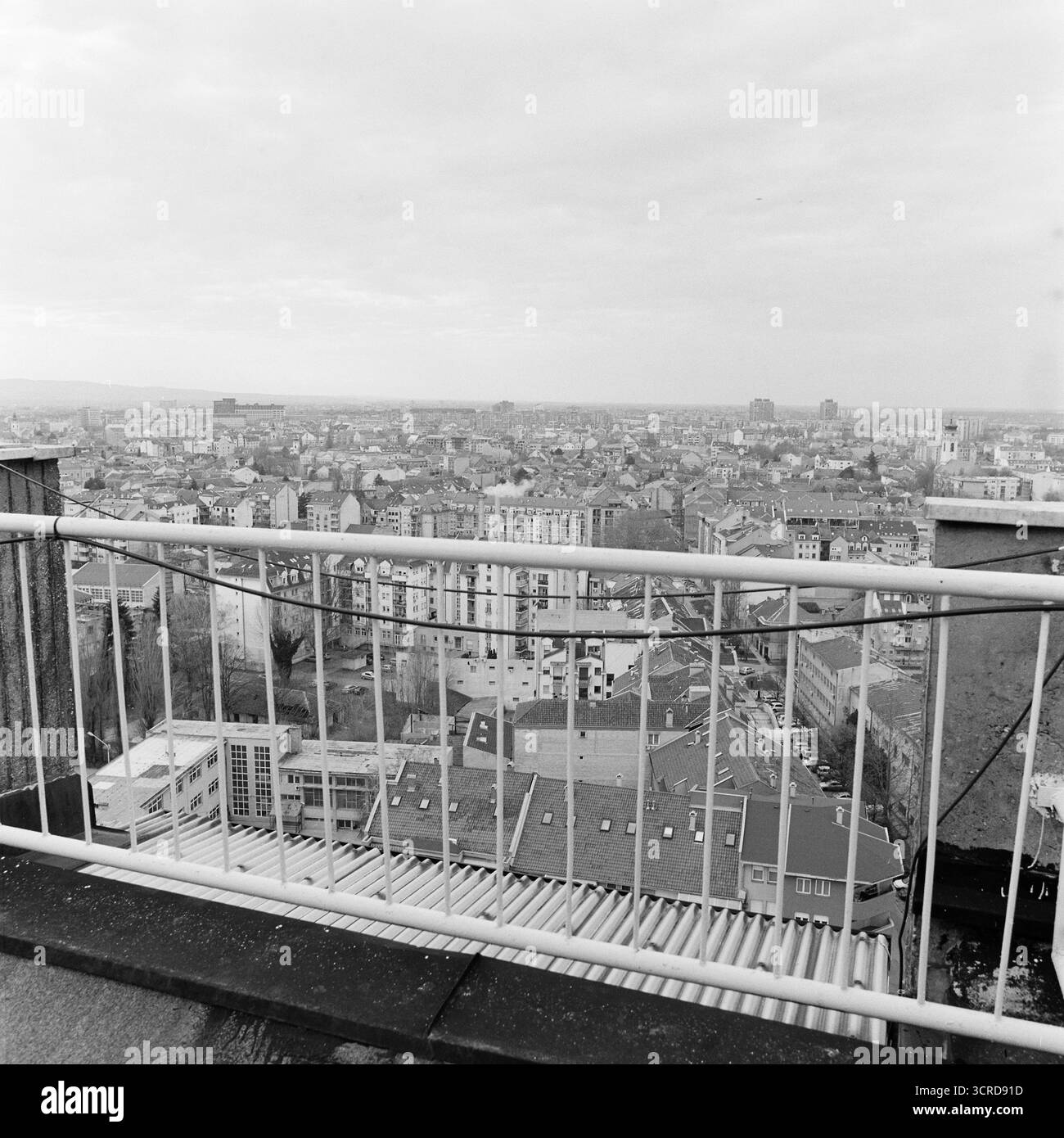 Photo en noir et blanc de Novi Sad depuis un toit de grande hauteur, avec garde-corps blanc au premier plan et paysage urbain s'étendant au loin. Banque D'Images