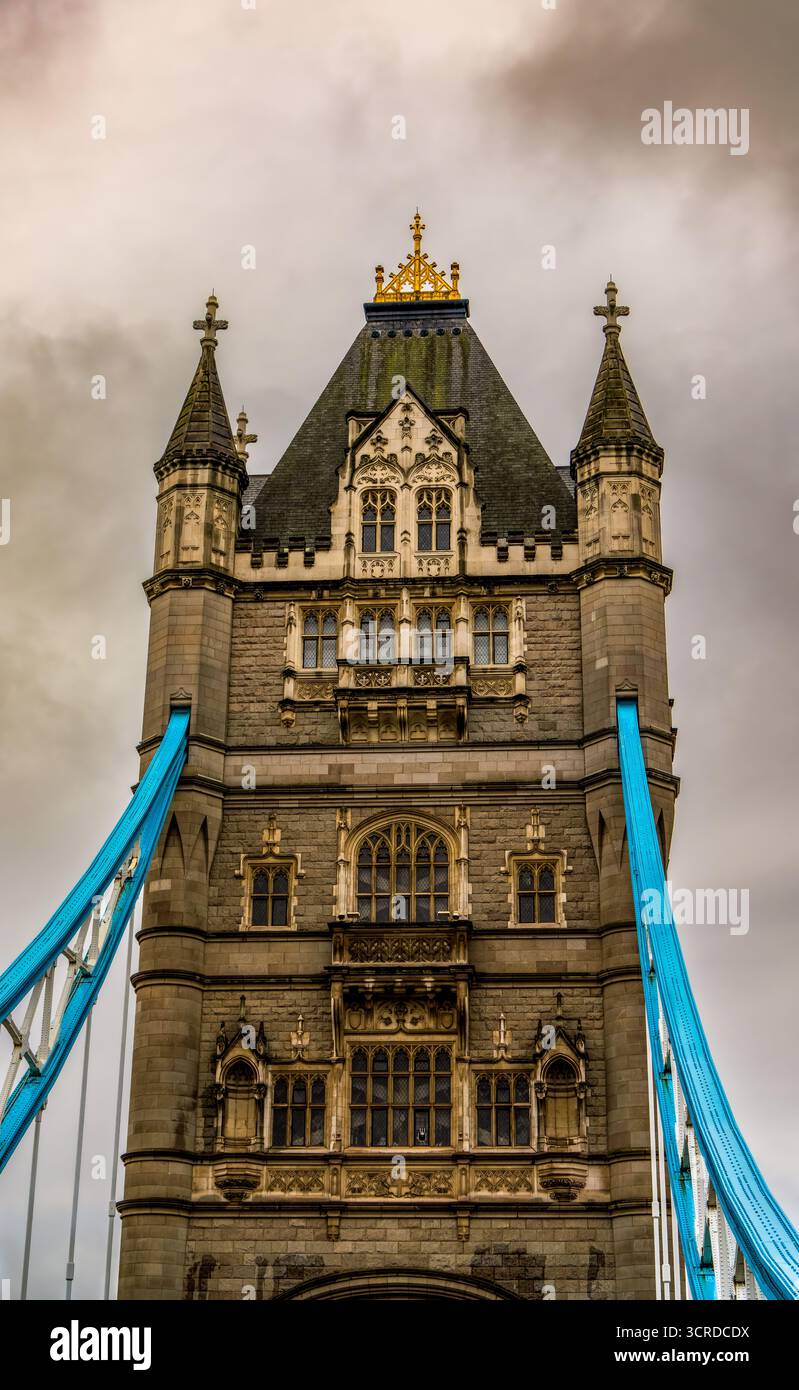 Tour emblématique de Tower Bridge à Londres avec architecture néo-gothique et câbles suspendus bleus sous un ciel nuageux spectaculaire Banque D'Images