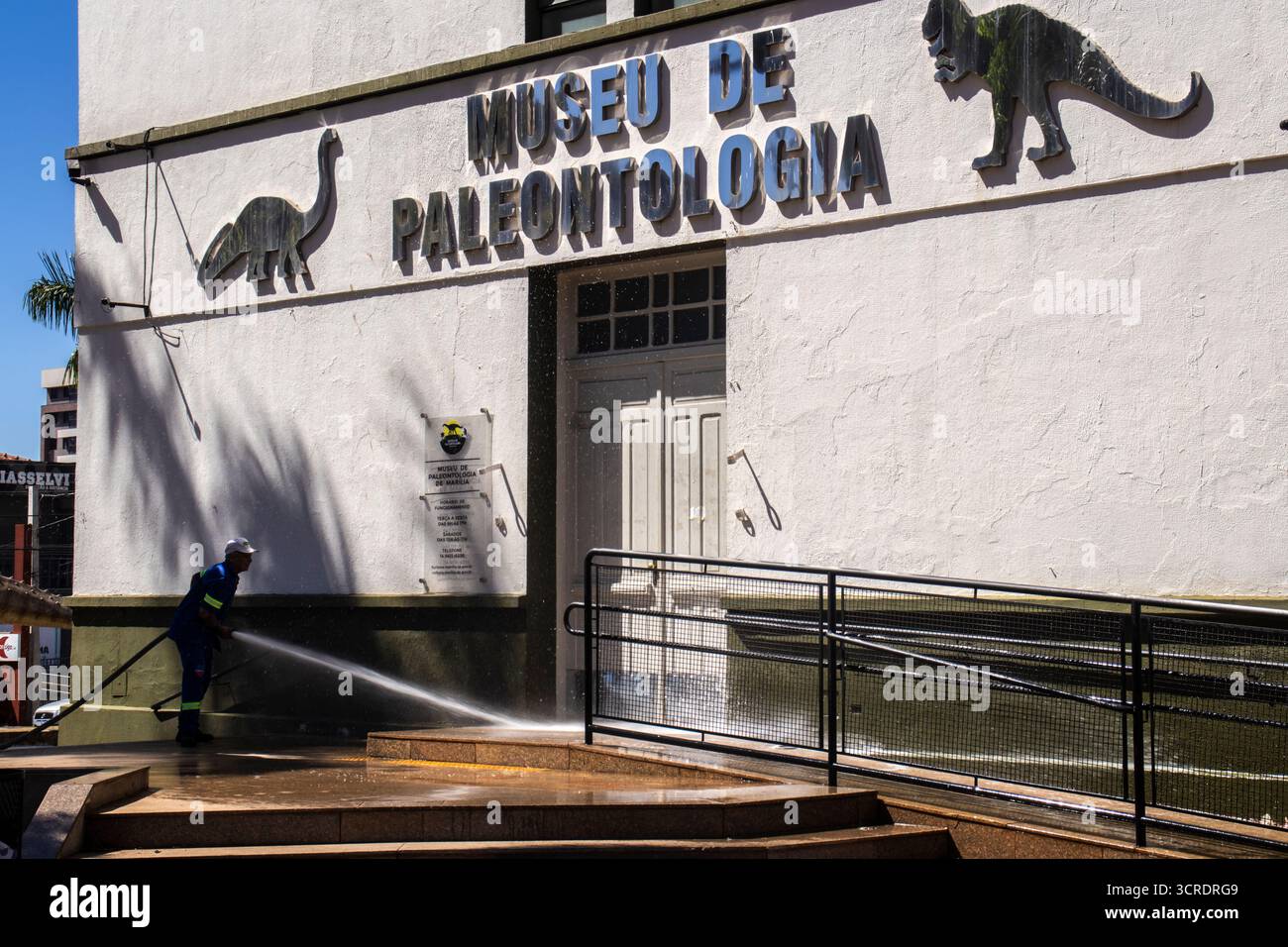 Marilia, SP, Brésil, 10 septembre 2025. Travailleur lavant le trottoir avec un tuyau devant le musée de paléontologie dans le centre-ville, soulignant ur Banque D'Images