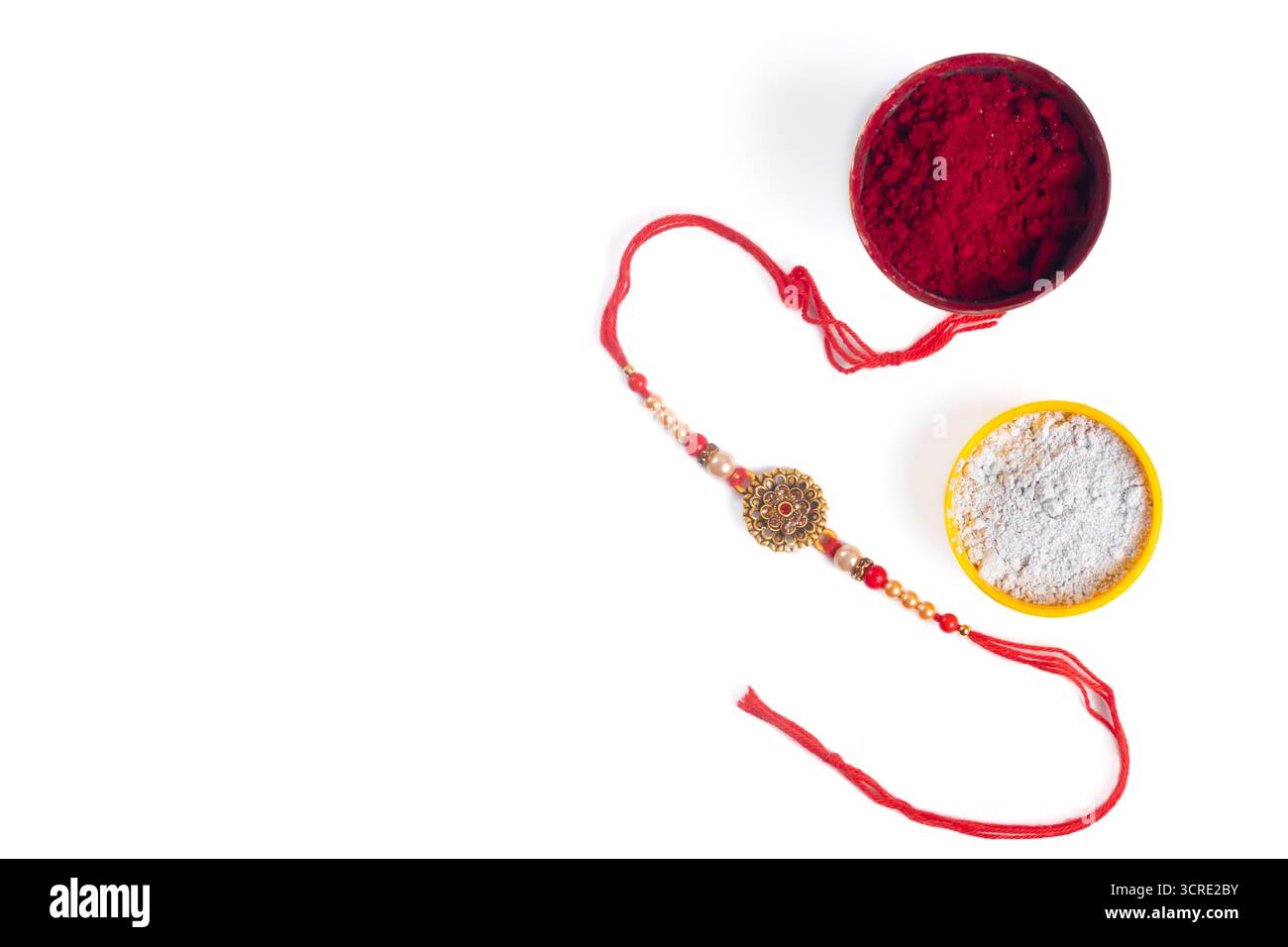 Un bracelet Rakhi vibrant avec du kumkum rouge et de la poudre blanche est affiché à côté de bols colorés. Cette scène festive capte les liens familiaux, tradit indien Banque D'Images