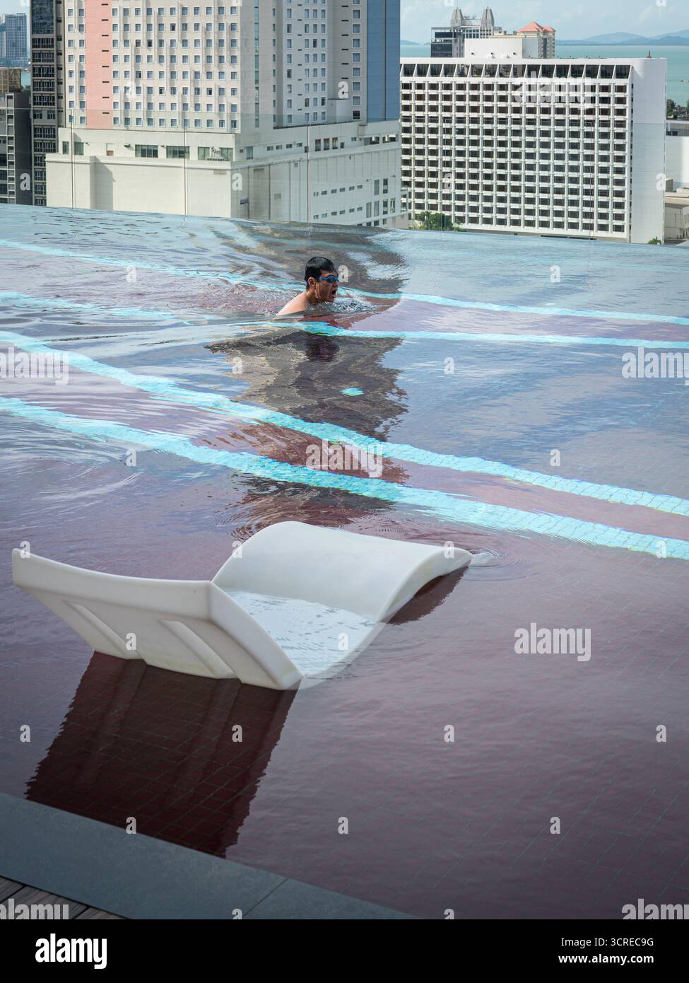 Homme nageant dans la piscine sur le toit à débordement, avec vue sur la ville à l'arrière-plan. Banque D'Images