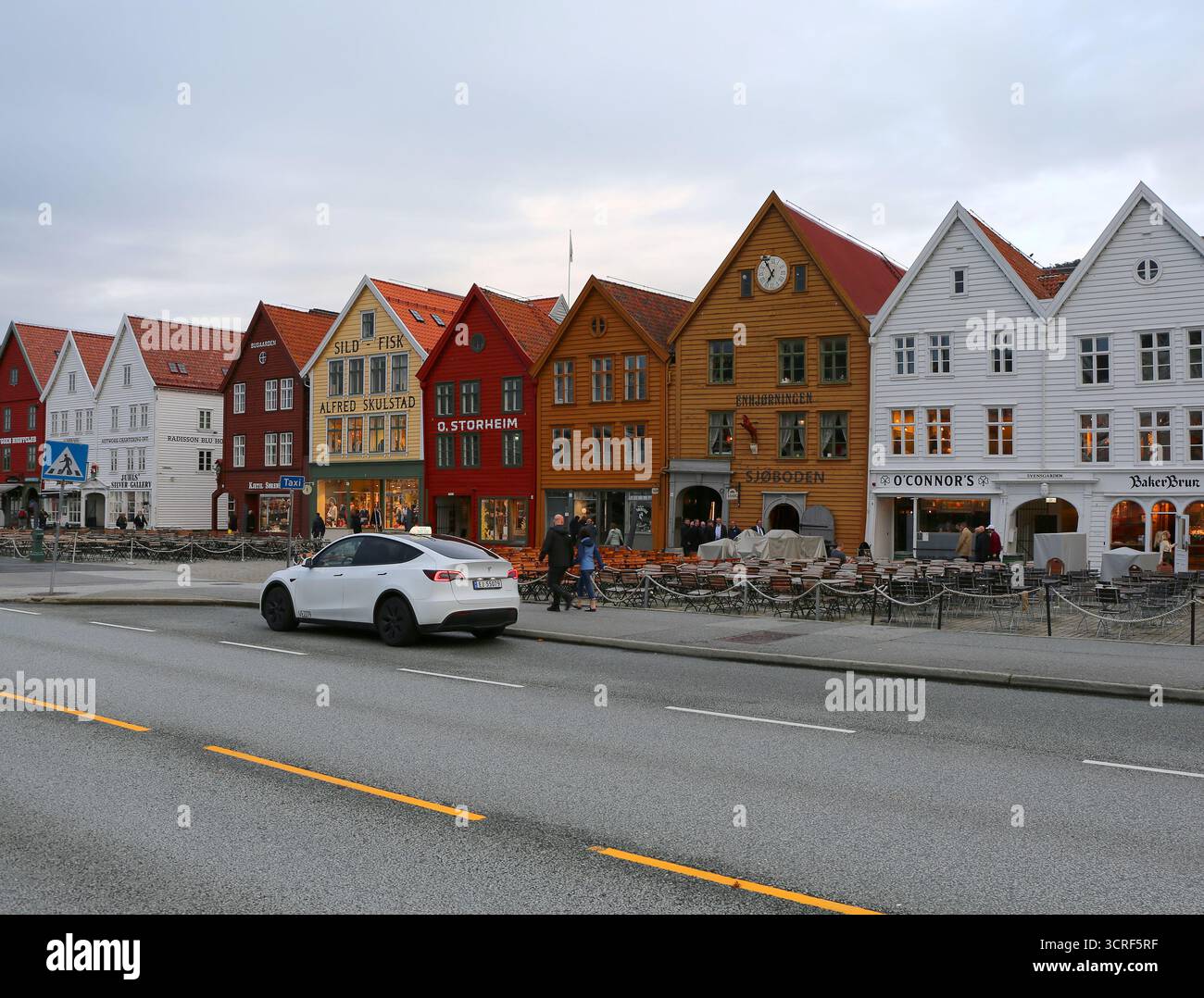 Bergen, Norvège-15 septembre 2025 : gens non identifiés marchant près des bâtiments historiques en bois colorés de Bryggen et attendant Tesla Taxi Banque D'Images