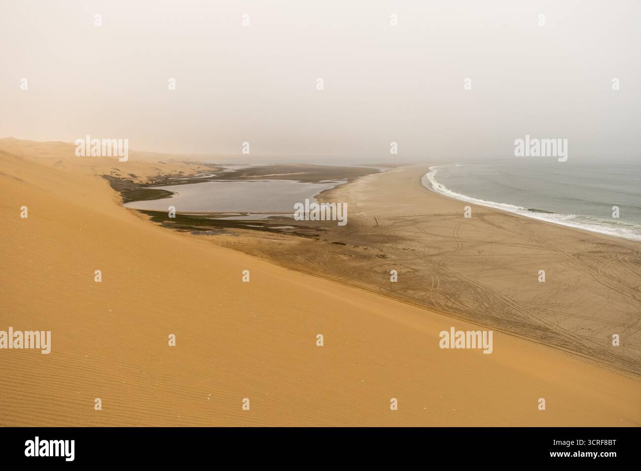 Dunes dorées et océan Atlantique près du parc Namib-Naukluft, Namibie. Un lagon et un rivage s'estompent dans la brume et le temps nuageux, créant un des spectaculaire Banque D'Images