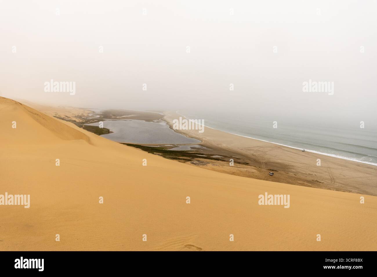Dunes dorées et océan Atlantique près du parc Namib-Naukluft, Namibie. Un lagon et un rivage s'estompent dans la brume et le temps nuageux, créant un des spectaculaire Banque D'Images