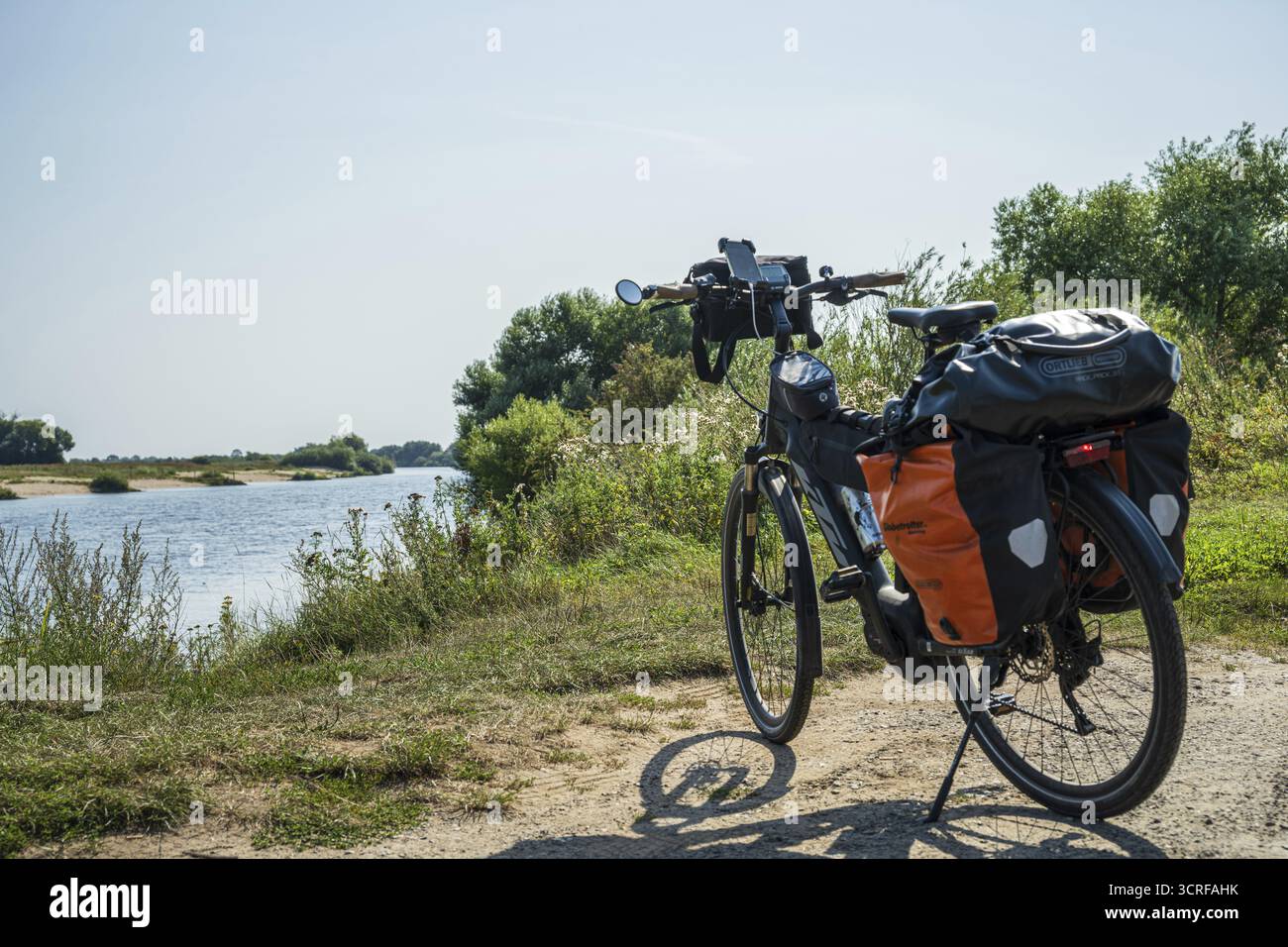 Un vélo avec valises se dresse sur une rive ensoleillée, encastrée dans la nature, piste cyclable Weser, Weser, vélo de tourisme Banque D'Images