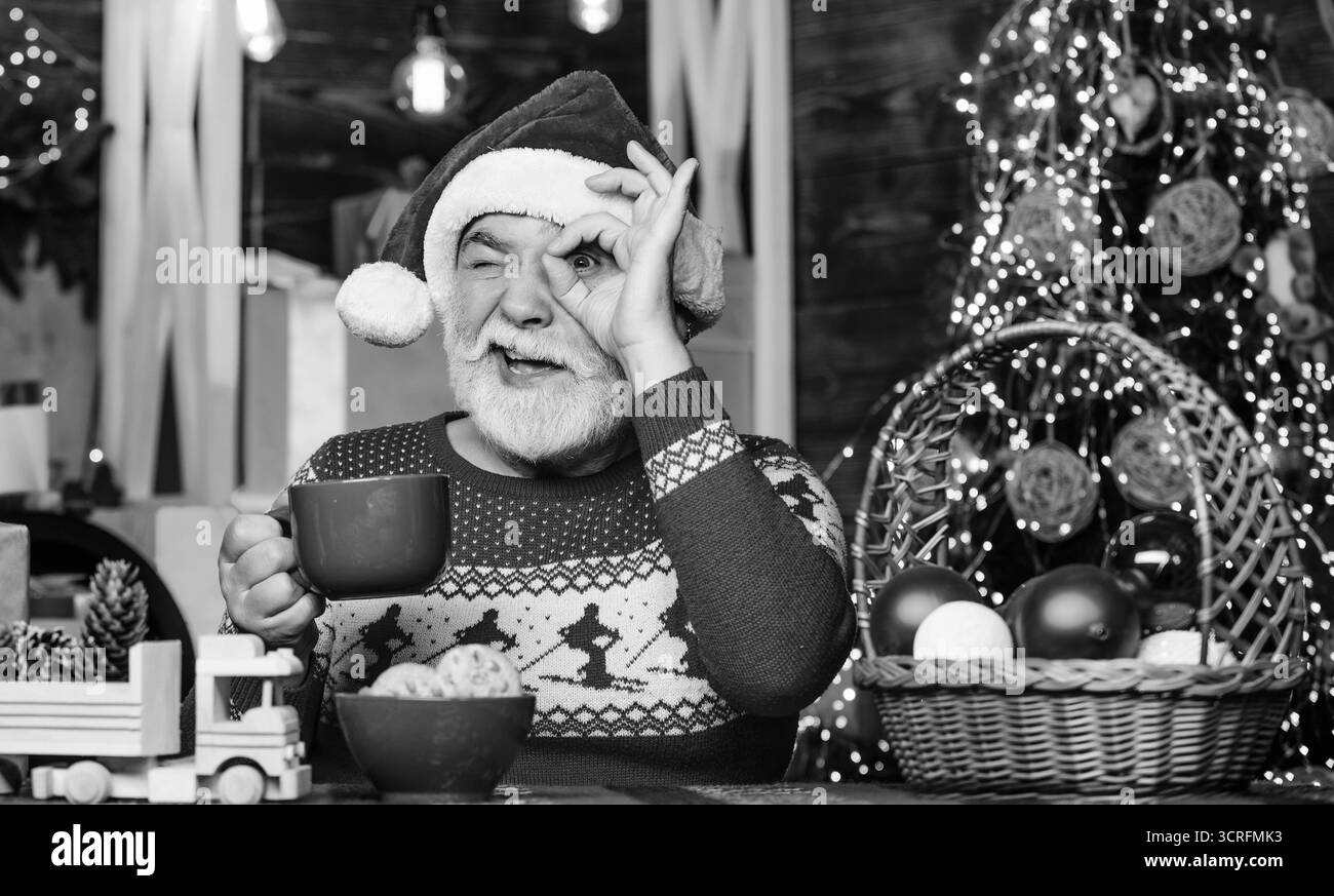 Père noël homme senior buvant du thé. Nouvel an. Grand-père avec mug. Intérieur confortable. Friandises de la veille de Noël. Vacances d'hiver. Recette de cacao de Noël. Guirlande Banque D'Images