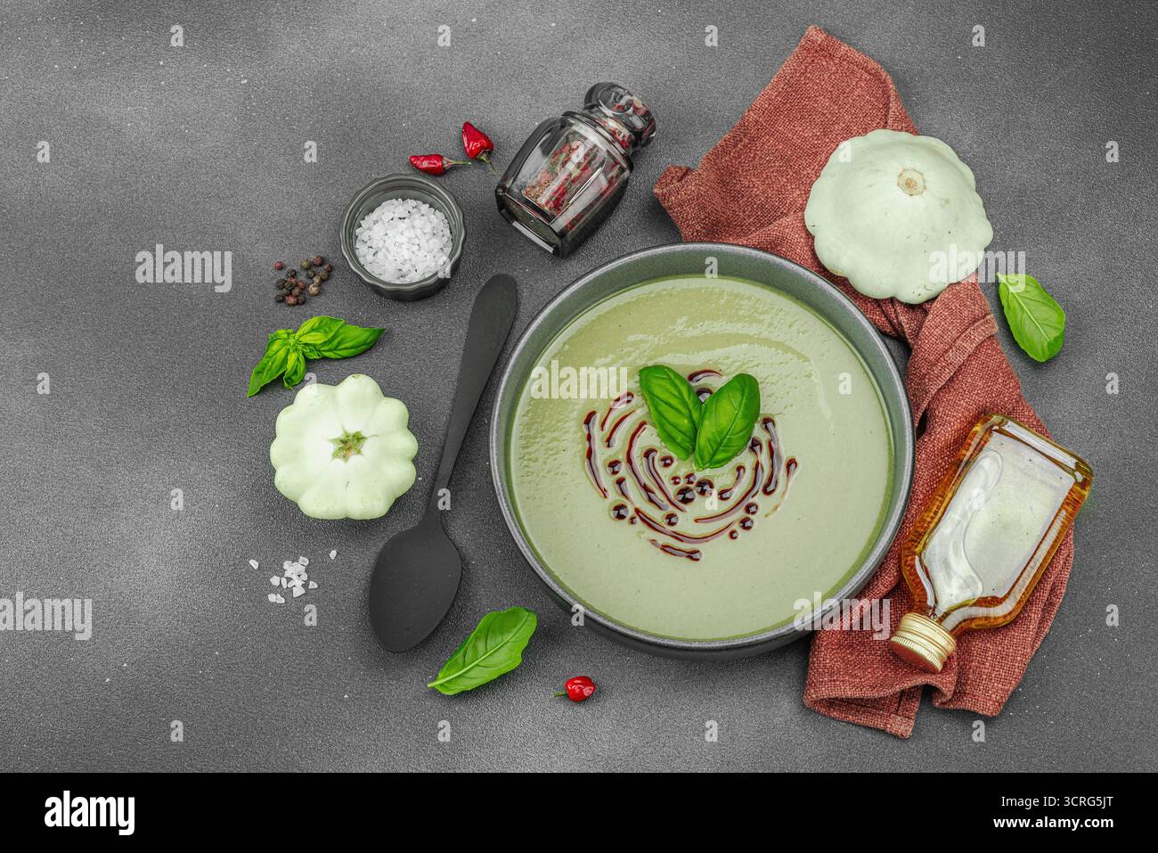 Soupe crémeuse à la courge pattypan, garnie de basilic et de glaçage balsamique, servie dans un bol tendance avec des ingrédients frais et des épices. Béton de pierre sombre b Banque D'Images