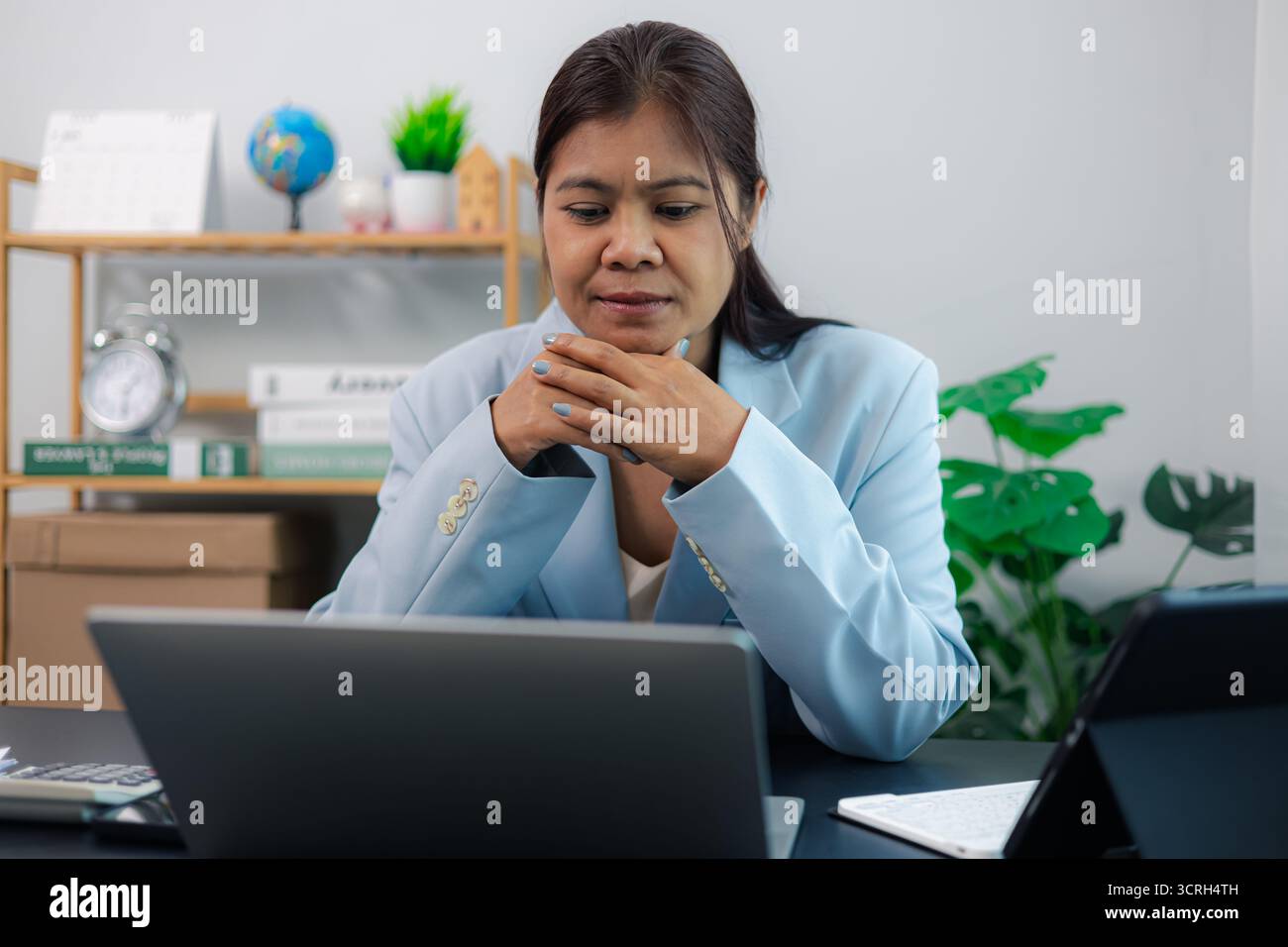 Femme d'affaires asiatique concentrée repose menton sur les mains serrées tout en se concentrant sur l'ordinateur portable dans le bureau à domicile moderne. Femme professionnelle montre le dévouement et p Banque D'Images