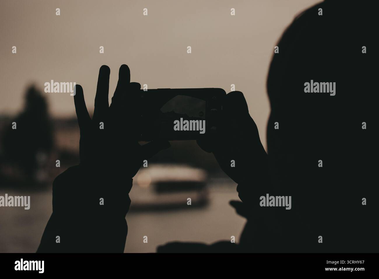 Silhouette d'une personne prenant une photo d'un bâtiment avec un smartphone. Une personne est silhouettée sur un fond flou, tenant un téléphone pour capturer Banque D'Images