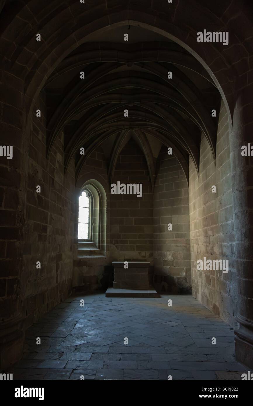 Vue intérieure d'une chambre d'église sombre avec fenêtre gothique, la lumière brille aux murs sous un plafond voûté. Concentrez-vous sur un piédestal vide au centre Banque D'Images