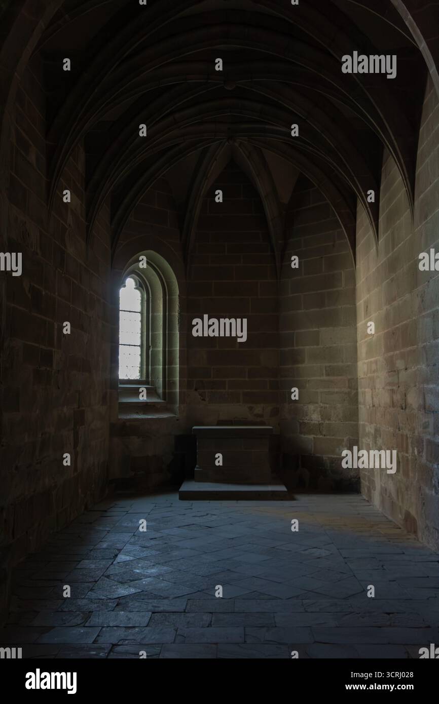 Vue intérieure d'une chambre d'église sombre avec fenêtre gothique, la lumière brille aux murs sous un plafond voûté. Concentrez-vous sur un piédestal vide au centre Banque D'Images