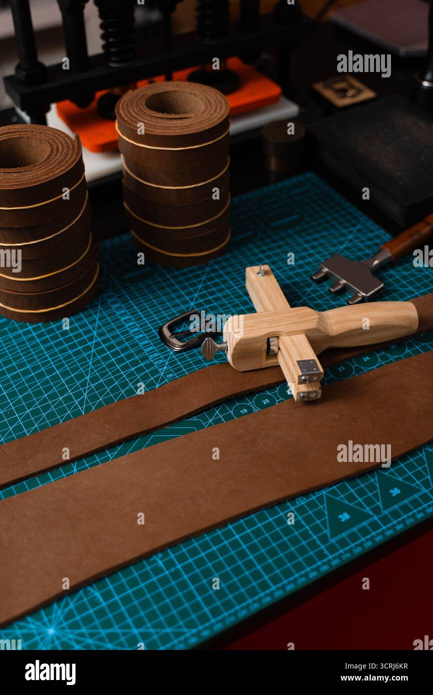 Installation de travail du cuir avec des outils, une boucle et des bandes de cuir disposées soigneusement sur un tapis, prêt pour la fabrication de ceinture. Outils de maroquinerie et fabrication de courroies p Banque D'Images