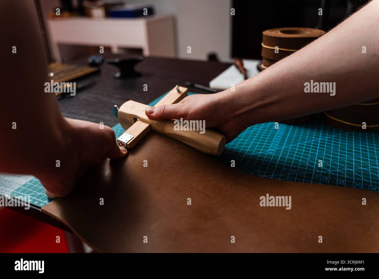 Artisan préparant le bracelet en cuir à l'aide d'un couteau en bois sur le tapis. Préparation de ceinture en cuir à la main avec coupe-sangle en bois sur le tapis de coupe. Artisan est Cu Banque D'Images