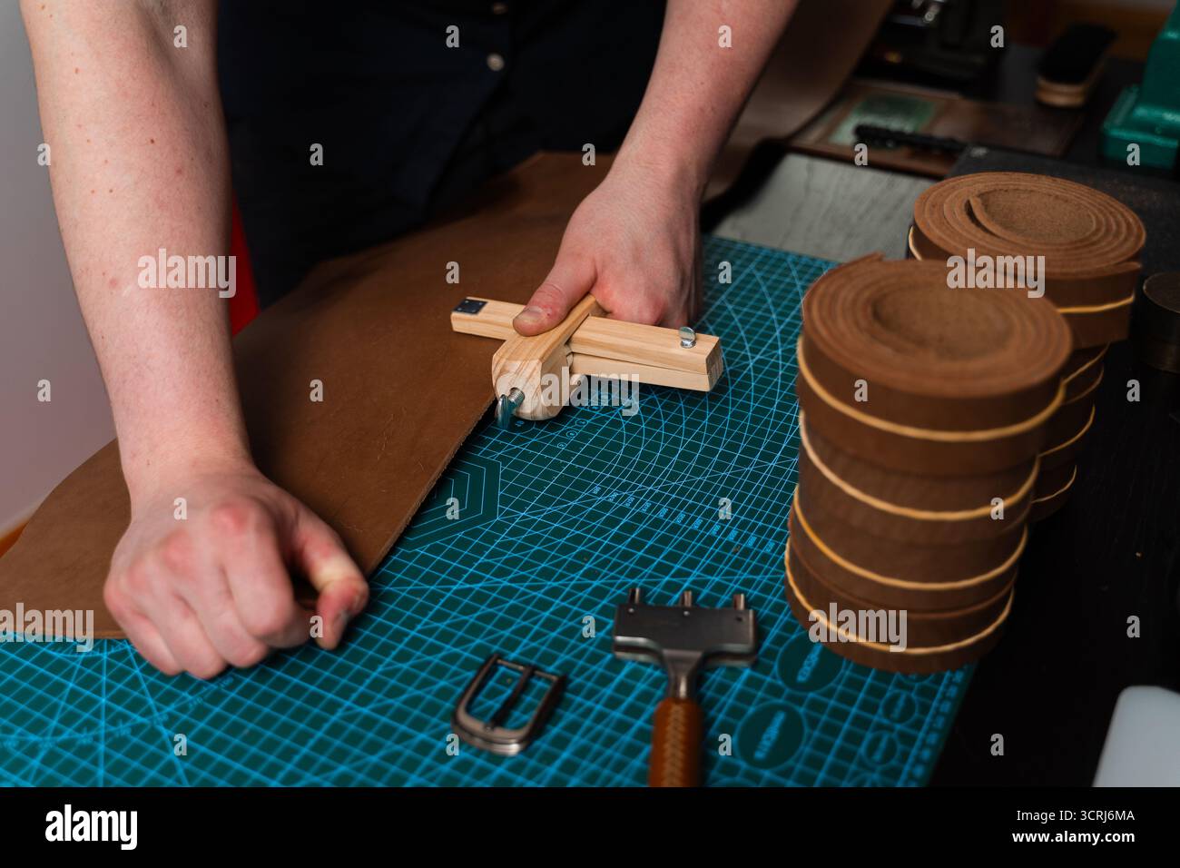 Artisan préparant le bracelet en cuir à l'aide d'un couteau en bois sur le tapis. Préparation de ceinture en cuir à la main avec coupe-sangle en bois sur le tapis de coupe. Artisan est Cu Banque D'Images