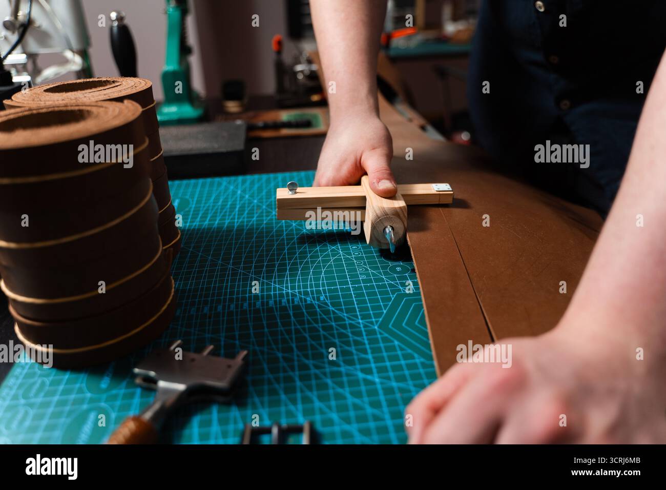 Artisan préparant le bracelet en cuir à l'aide d'un couteau en bois sur le tapis. Préparation de ceinture en cuir à la main avec coupe-sangle en bois sur le tapis de coupe. Artisan est Cu Banque D'Images