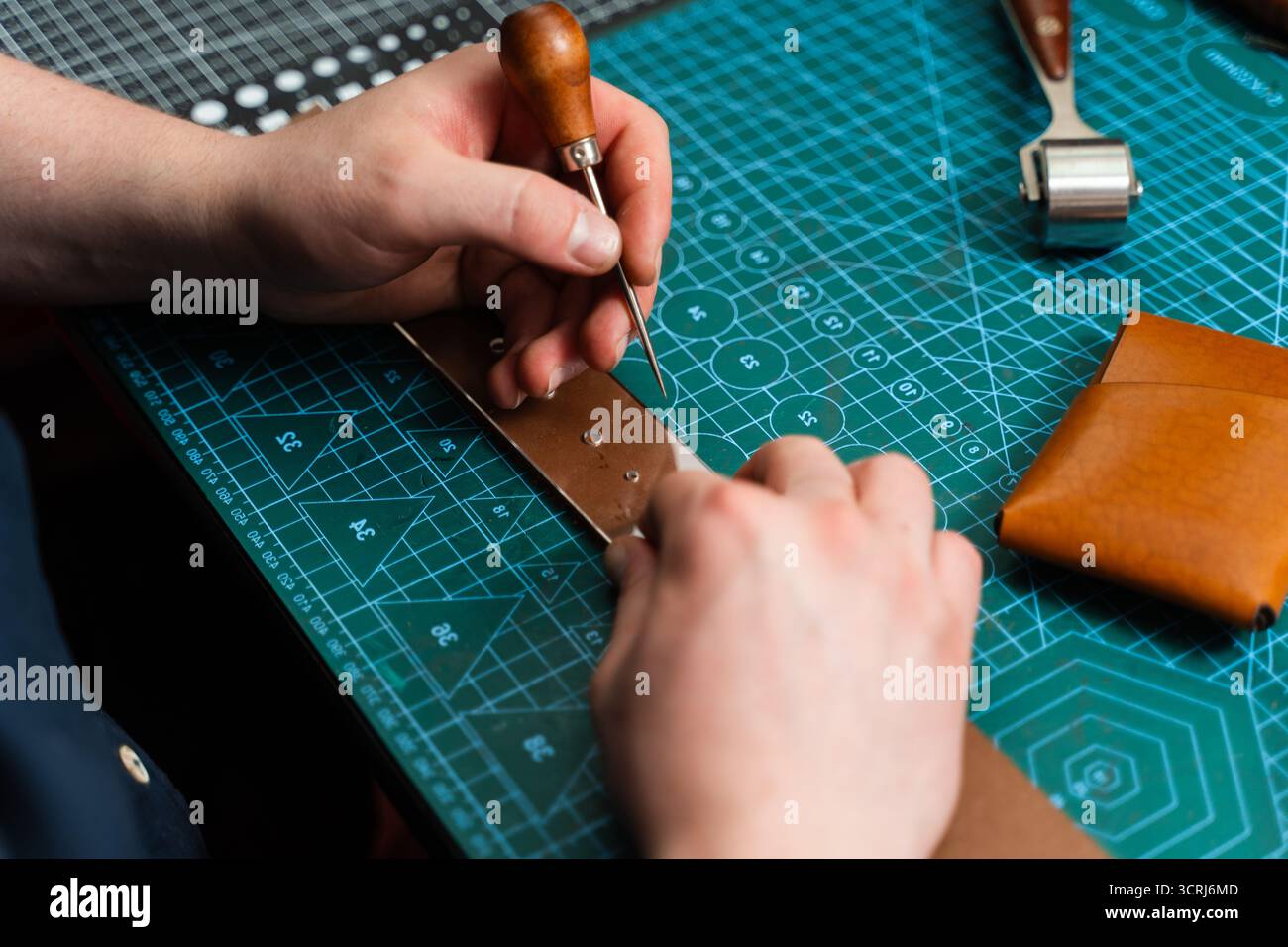 Fabrication de trous de ceinture avec outil de poinçon sur bracelet en cuir. Poinçonnage et détail des trous de ceinture en cuir. Artisan perçant des trous dans un bracelet en cuir pour un han Banque D'Images