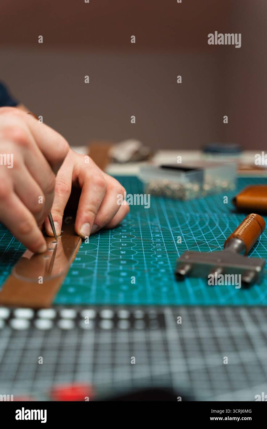 Fabrication de trous de ceinture avec outil de poinçon sur bracelet en cuir. Poinçonnage et détail des trous de ceinture en cuir. Artisan perçant des trous dans un bracelet en cuir pour un han Banque D'Images