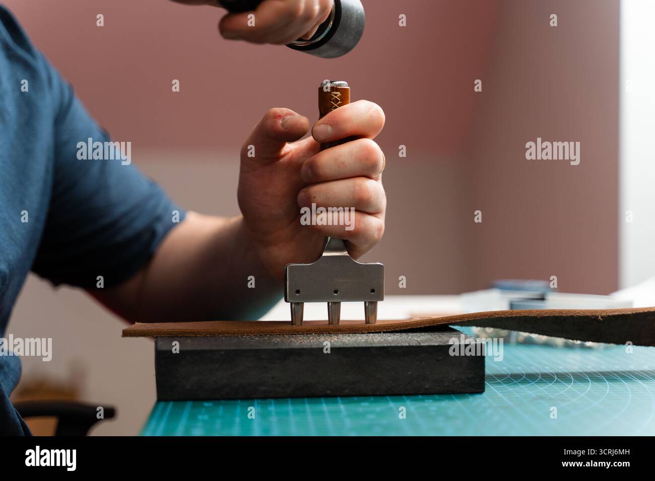 Fabrication de trous de ceinture avec outil de poinçon sur bracelet en cuir. Poinçonnage et détail des trous de ceinture en cuir. Artisan perçant des trous dans un bracelet en cuir pour un han Banque D'Images