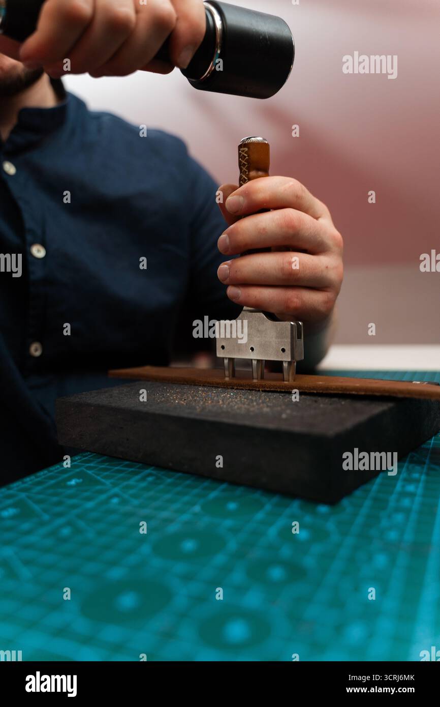 Fabrication de trous de ceinture avec outil de poinçon sur bracelet en cuir. Poinçonnage et détail des trous de ceinture en cuir. Artisan perçant des trous dans un bracelet en cuir pour un han Banque D'Images