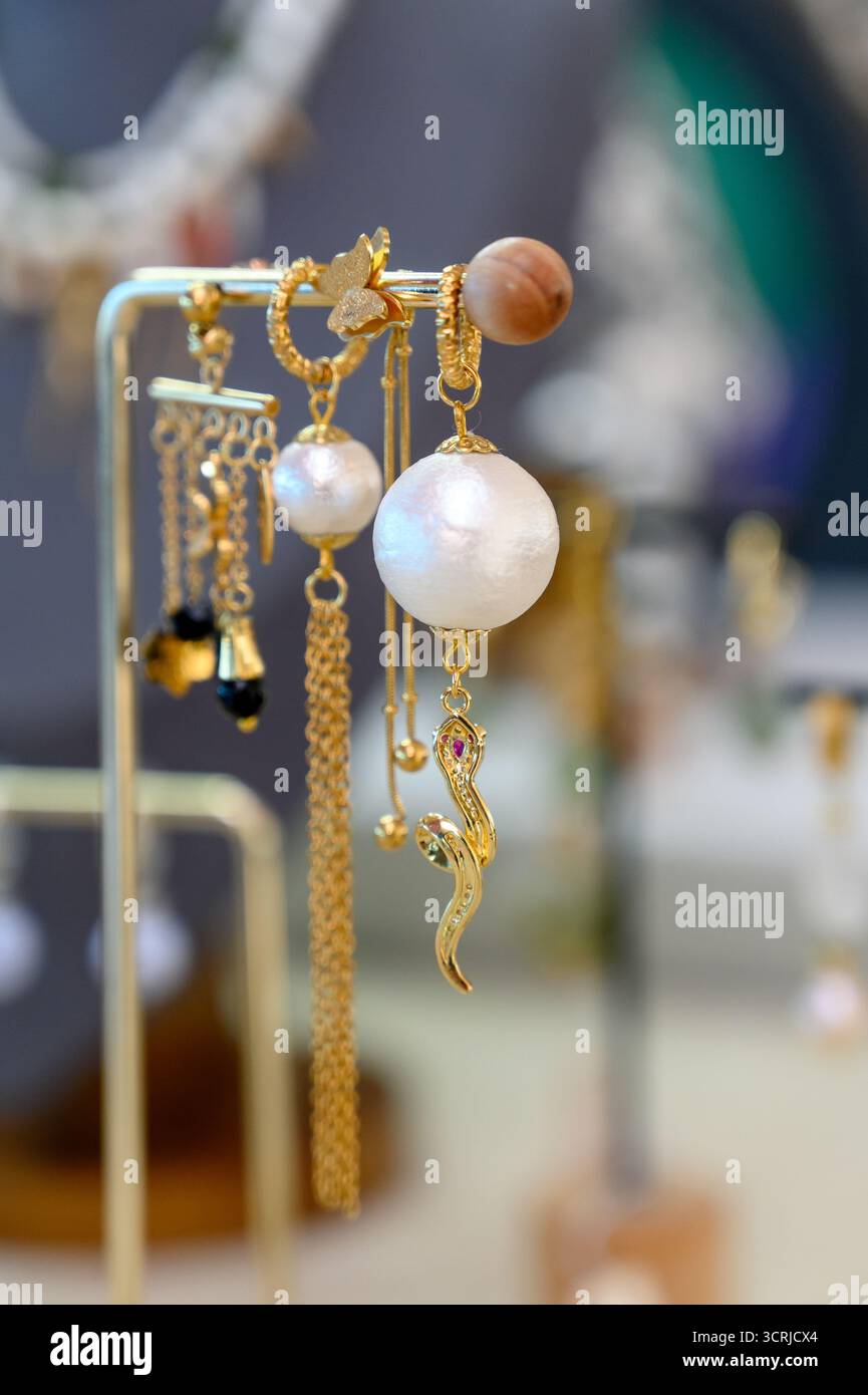 Une collection de boucles d'oreilles fabriquées à la main sur un support de bijoux plaqué or.boucles d'oreilles assorties perlées et en pierre à vendre Banque D'Images