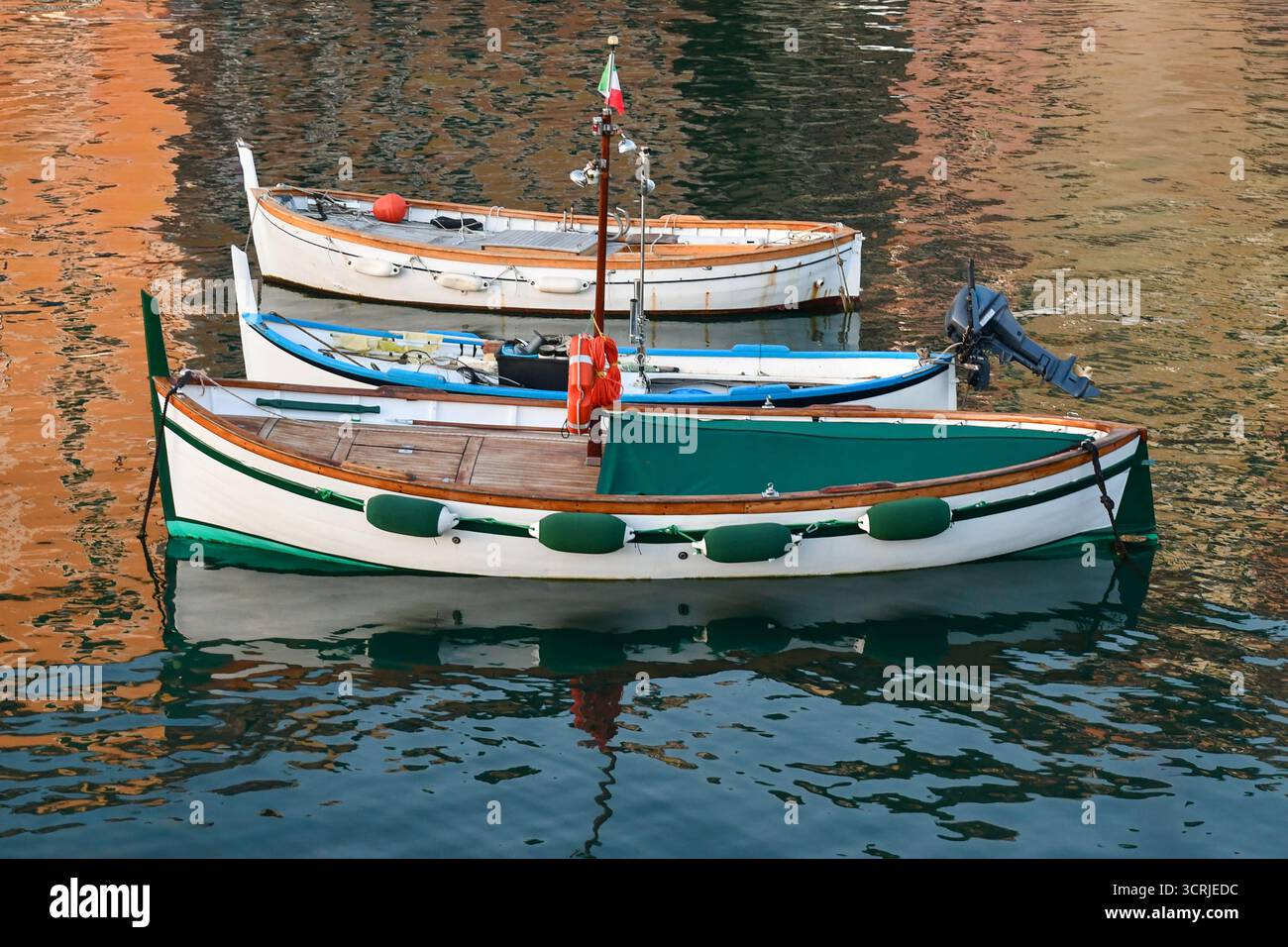 Trois petits bateaux de pêche ancrés dans le port avec des reflets d'eau au coucher du soleil, Camogli (Gênes), Ligurie, Italie Banque D'Images