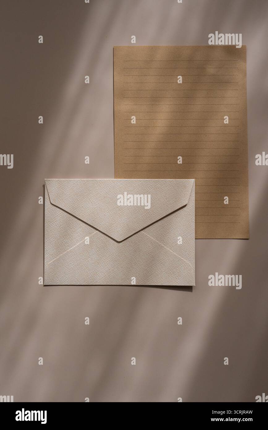 Enveloppe beige et feuille de papier kraft. Set de papeterie minimaliste avec une enveloppe texturée beige et une feuille de papier kraft doublée sur un fond beige avec Banque D'Images